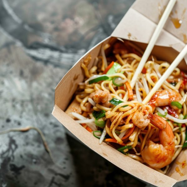 Wok noodles with shrimps and vegetables in take away box on dark background